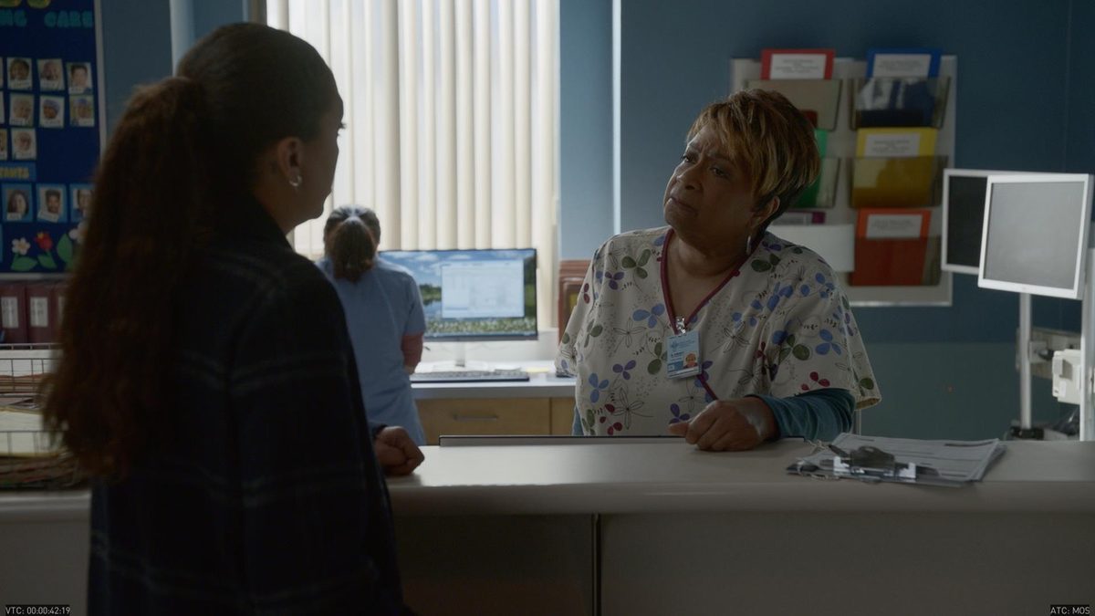 The nurses’ station. Chart racks, pinned notices and the staff board, all reading as background.
