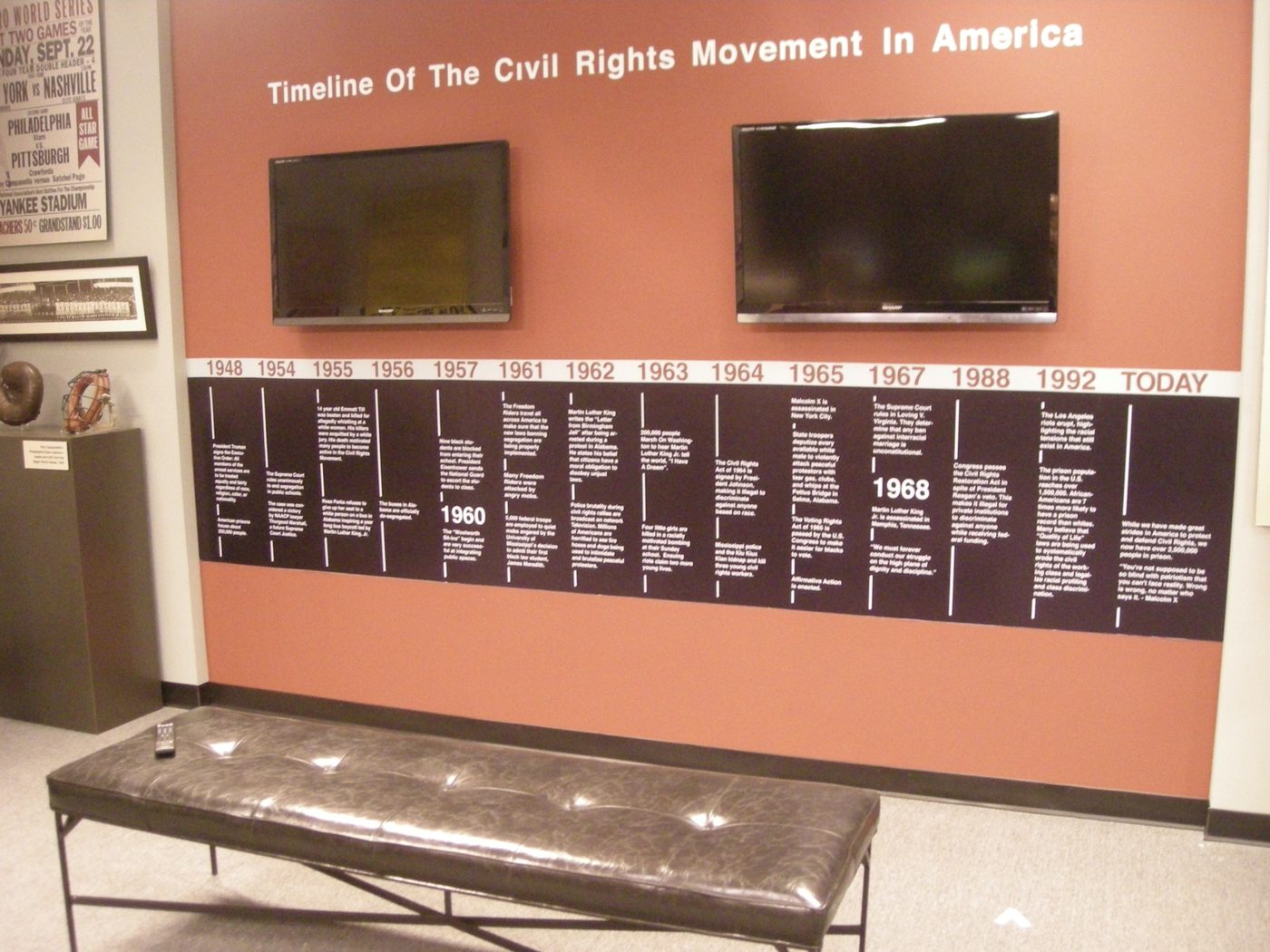 Year by year across the full wall, in white on black, with two screens set into the run.
