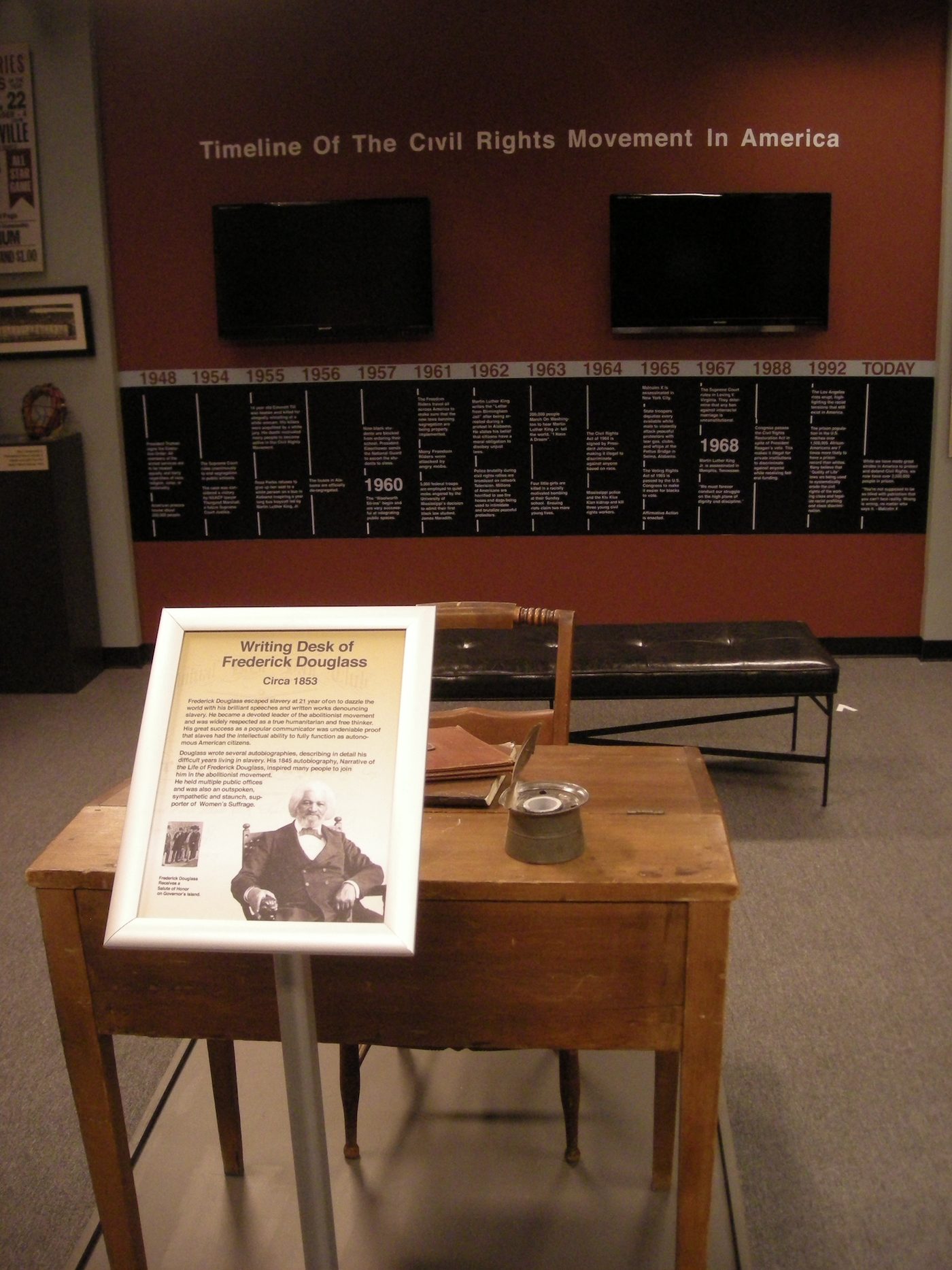 The same wall from the room, with a writing desk and its interpretive label in the foreground.
